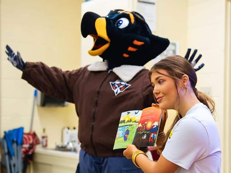 Woman reading book beside Captain Skyhawk mascot