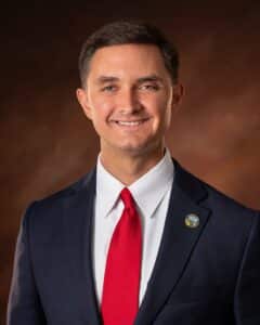 Headshot of a man in a suit with a red tie.