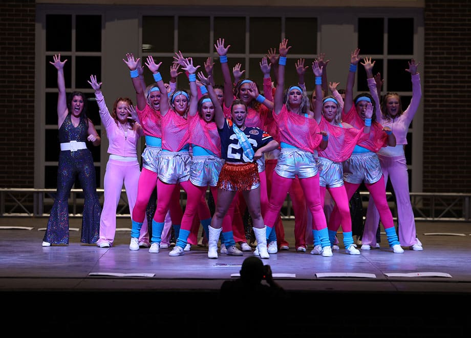 Students dressed in colorful outfits perform on stage.