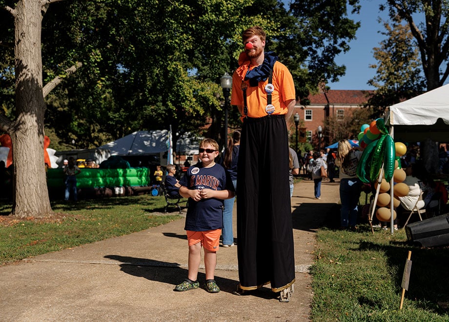 A person on stilts dressed as a clown poses with a kid during Quad City.