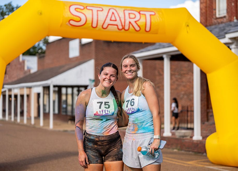 Two women in activewear stand under a yellow arch with the word Start.