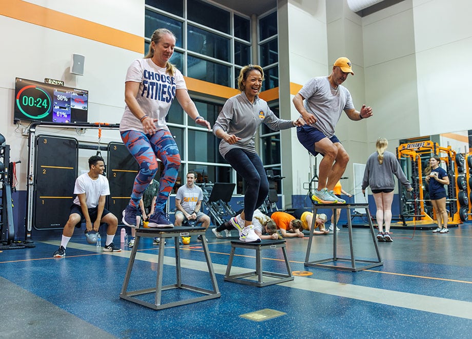 Three adults stand on stools in a workout room.