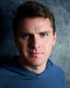 Headshot of a man with brown hair and a navy top.